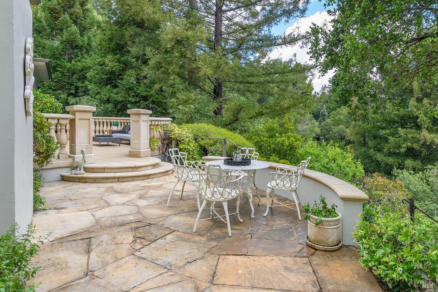 Stone terrace with iron furniture and balustraded edge overlooking redwoods